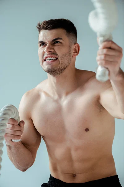 Sexy muscular bodybuilder with bare torso exercising with battle rope isolated on grey — Stock Photo