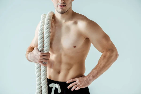 Cropped view of sexy muscular bodybuilder with bare torso posing with battle rope isolated on grey — Stock Photo