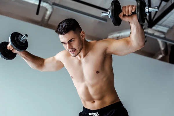 Vista de ángulo bajo del musculoso tenso culturista con torso desnudo haciendo ejercicio con pesas - foto de stock