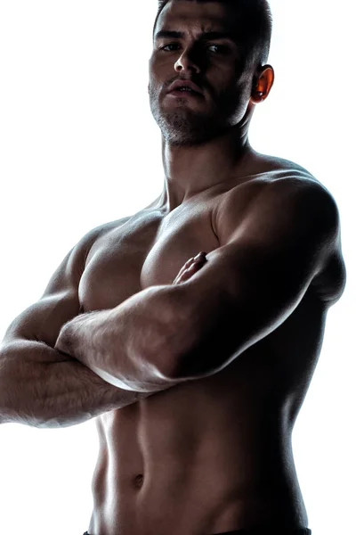 Bodybuilder musclé sexy avec torse nu posant avec les bras croisés dans l'ombre isolé sur blanc — Photo de stock