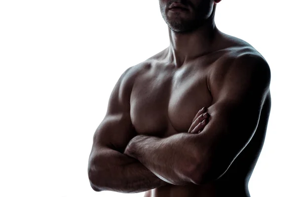 Cropped view of sexy muscular bodybuilder with bare torso posing with crossed arms in shadow isolated on white — Stock Photo