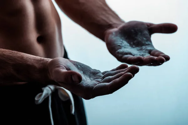 Ausgeschnittene Ansicht eines sexy muskulösen Bodybuilders mit nacktem Oberkörper, der Talkumpuder auf weiße Hände aufträgt — Stockfoto