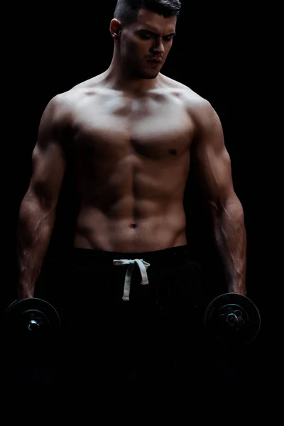 Sexy muscular bodybuilder with bare torso excising with dumbbells isolated on black — Stock Photo