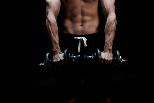 Partial view of sexy muscular bodybuilder with bare torso excising with dumbbells isolated on black — Stock Photo