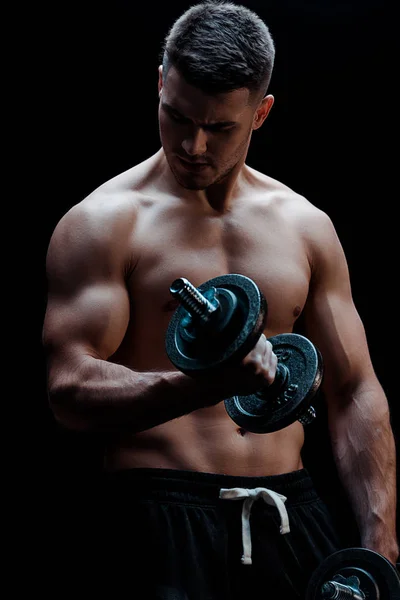 Sexy muscular bodybuilder with bare torso excising with dumbbell isolated on black — Stock Photo