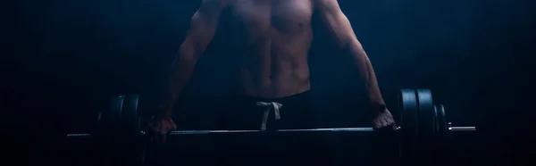 Ausgeschnittene Ansicht von sexy muskulösen Bodybuilder mit nacktem Oberkörper beim Schneiden mit Langhantel auf schwarzem Hintergrund mit Rauch, Panoramaaufnahme — Stockfoto