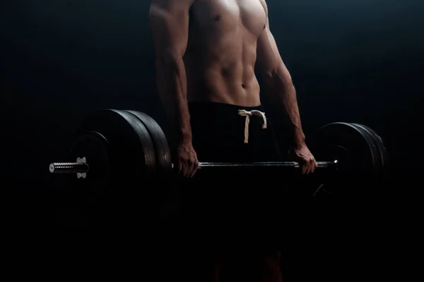 Cropped view of sexy muscular bodybuilder with bare torso excising with barbell isolated on black — Stock Photo