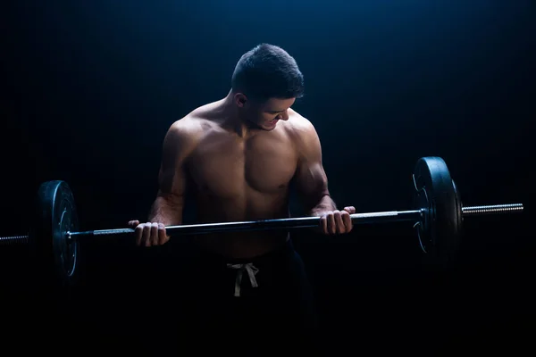 Musclé bodybuilder sexy avec torse nu excitant avec haltère sur fond noir avec de la fumée — Photo de stock