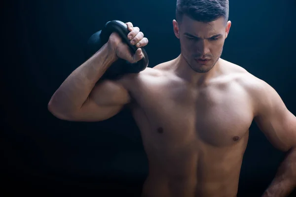 Sexy muscular bodybuilder with bare torso excising with kettlebell on black background — Stock Photo