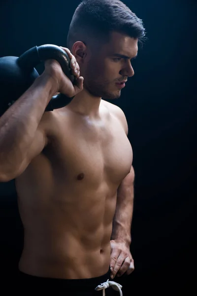 Sexy muscular bodybuilder with bare torso excising with kettlebell on black background — Stock Photo