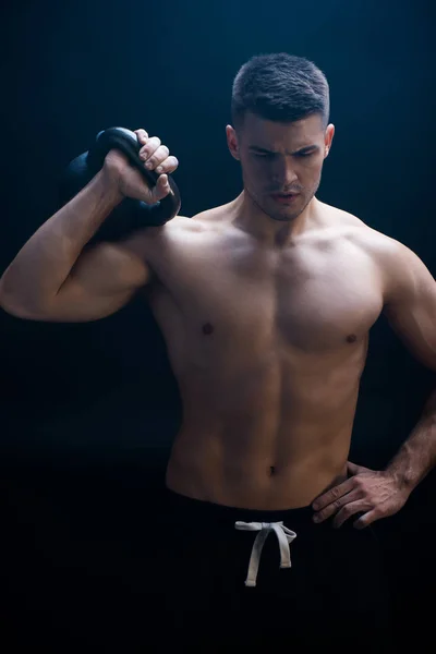 Sexy musculoso culturista con torso desnudo extirpando con kettlebell sobre fondo negro - foto de stock