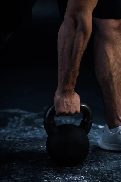 Cropped view of muscular bodybuilder excising with kettlebell on black — Stock Photo