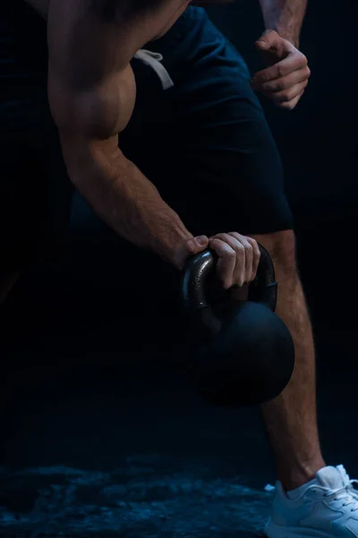 Recortado vista de sexy musculoso culturista extirpación con kettlebell sobre fondo negro - foto de stock