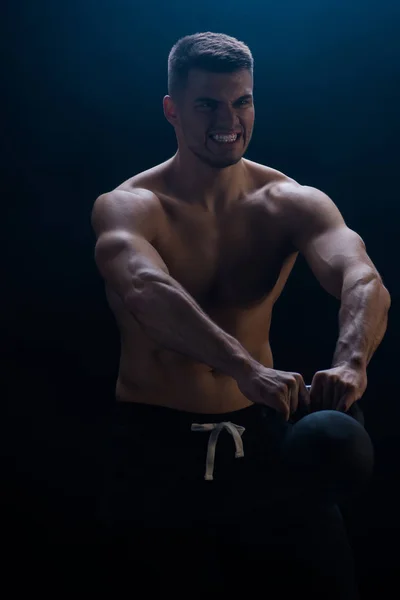 Tense sexy muscular bodybuilder with bare torso excising with kettlebell on black background — Stock Photo