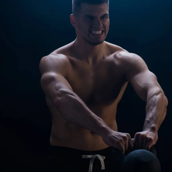 Tense sexy muscular bodybuilder with bare torso excising with kettlebell on black background — Stock Photo