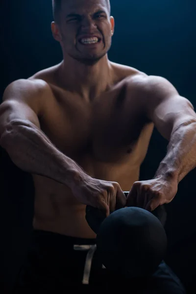 Tense sexy muscular bodybuilder with bare torso excising with kettlebell on black background — Stock Photo