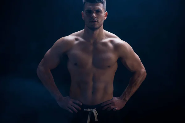 Sexy muscular bodybuilder with bare torso posing with hands on hips on black background — Stock Photo