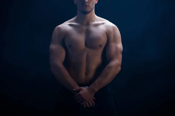 Recortado vista de sexy musculoso culturista con torso desnudo posando sobre fondo negro - foto de stock