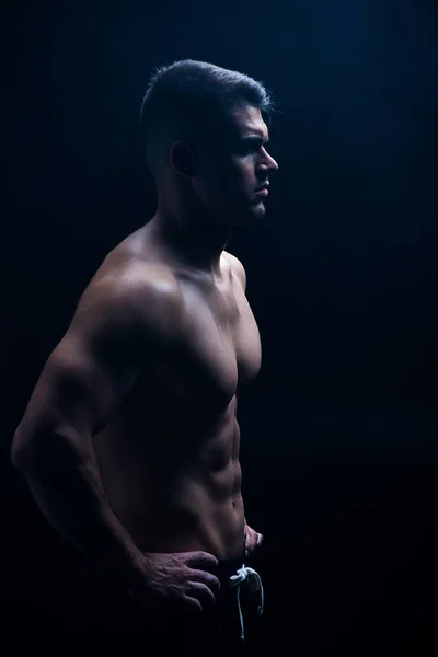 Vue latérale du bodybuilder musclé sexy avec torse nu posant avec les mains sur les hanches isolées sur noir — Photo de stock