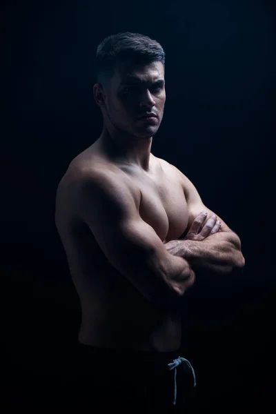 Sexy musculoso culturista con torso desnudo posando con brazos cruzados aislados en negro - foto de stock