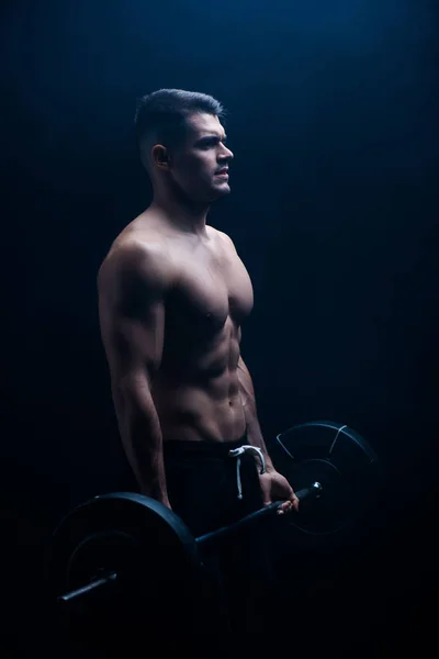 Sexy muscular bodybuilder with bare torso excising with barbell on black background — Stock Photo