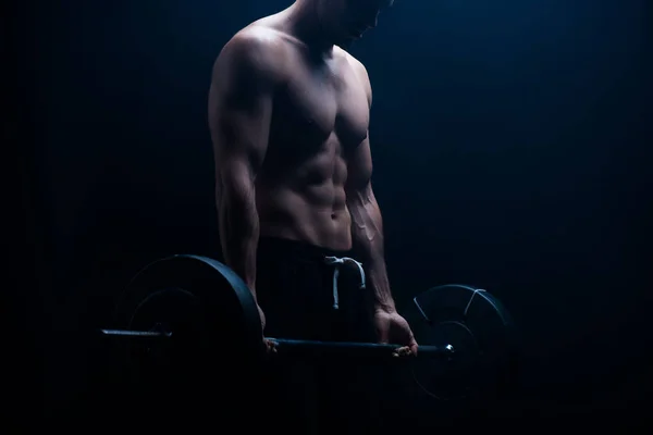 Vista recortada de musculoso culturista con torso desnudo extirpando con barra sobre fondo negro - foto de stock