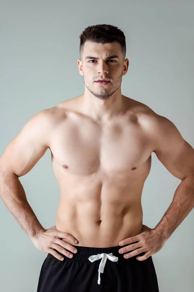 Sexy muscular bodybuilder with bare torso posing with hands on hips isolated on grey — Stock Photo