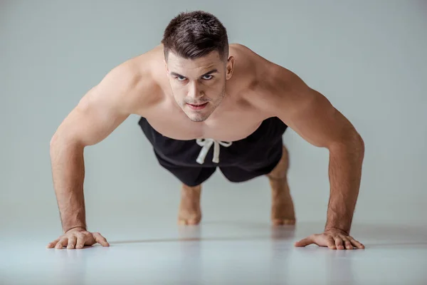 Сексуальный мускулистый спортсмен с голым туловищем, отжимающийся на сером — стоковое фото