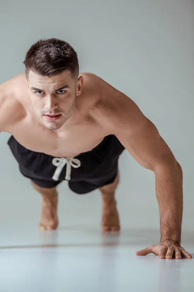 Sexy muscular sportsman with bare torso doing push ups on grey — Stock Photo