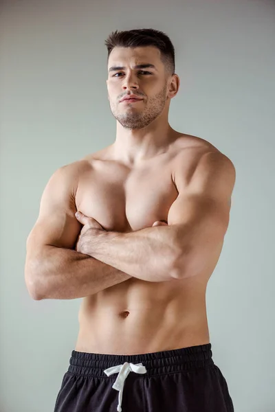 Sexy muscular bodybuilder with bare torso posing with crossed arms isolated on grey — Stock Photo