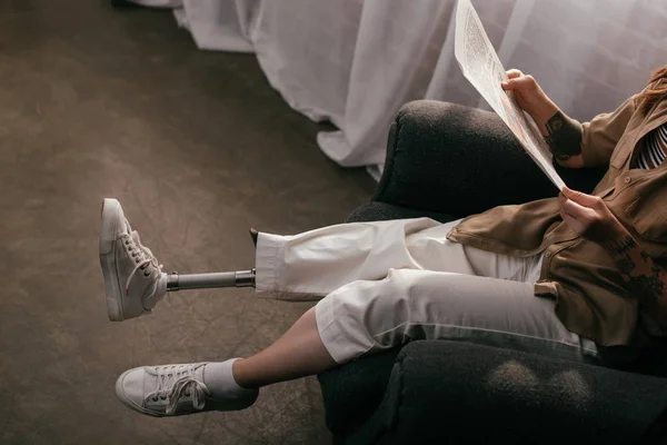 Cropped view of woman with prosthetic leg reading newspaper in armchair — Stock Photo