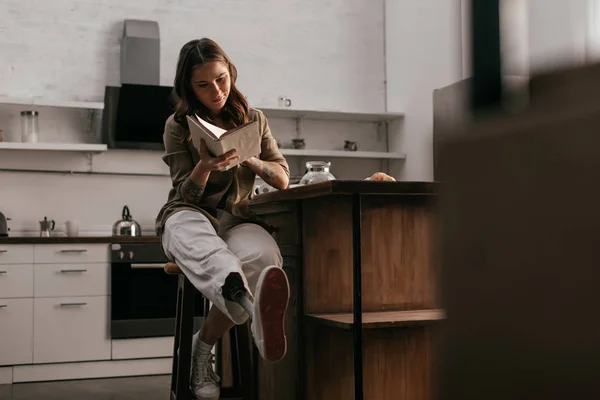 Foco seletivo da menina com prótese livro de leitura perna por mesa de cozinha — Fotografia de Stock