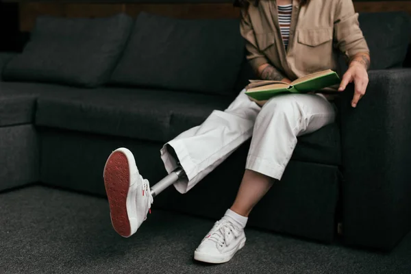 Обрізаний вид жінки з протезом для ніг читання книги на дивані — стокове фото