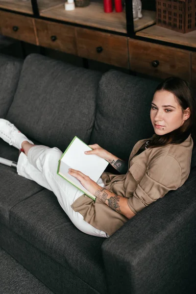 Vista ad alto angolo di ragazza con protesi gamba tenuta libro e guardando lontano sul divano — Foto stock