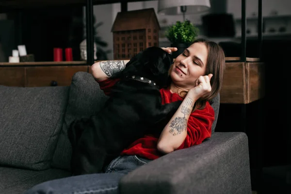 Красива дівчина з ампутованою ногою грає з мопсом собакою на дивані вдома — стокове фото