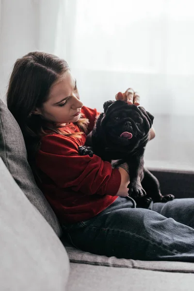 Side view of young woman stroking pug dog on sofa — Stock Photo