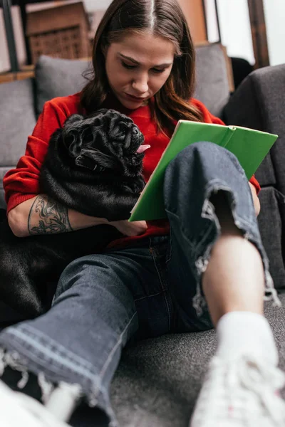 Selective focus of girl with leg prosthesis sitting on floor with pug and book — Stock Photo