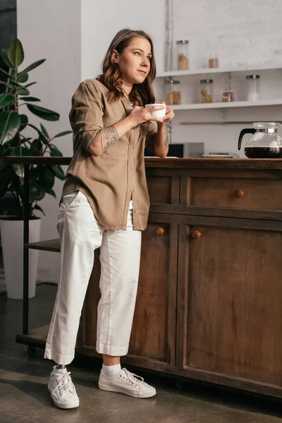 Mujer joven con la pierna protésica beber café por la mesa de la cocina - foto de stock