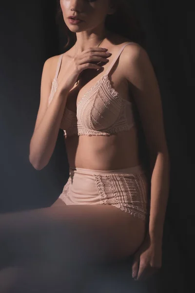 Abgeschnittene Ansicht einer sexy jungen Frau in Dessous posiert, während sie isoliert auf Schwarz sitzt — Stockfoto