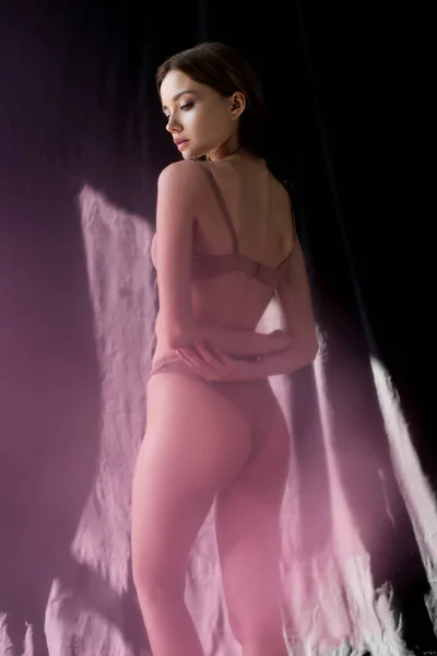 Sexy joven mujer en lencería de pie en la luz del sol en el fondo con negro cortina — Stock Photo