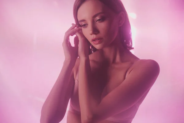Fille sensuelle en lingerie tenant les mains près du visage tout en posant sur fond rose et violet avec éclairage — Photo de stock