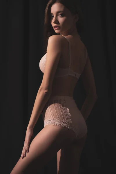 Seducente giovane donna in lingerie guardando la fotocamera mentre in piedi su sfondo nero — Foto stock