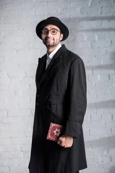 Handsome and smiling jewish man in glasses holding tanakh — Stock Photo