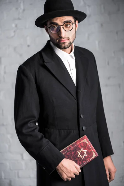Handsome and sad jewish man in glasses holding tanakh — Stock Photo
