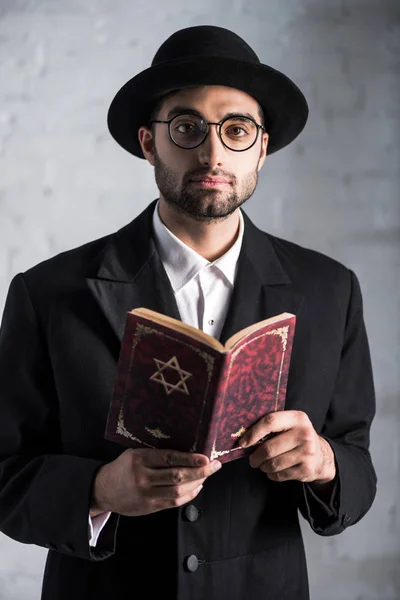 Bonito e jovem judeu homem em óculos segurando tanakh — Fotografia de Stock