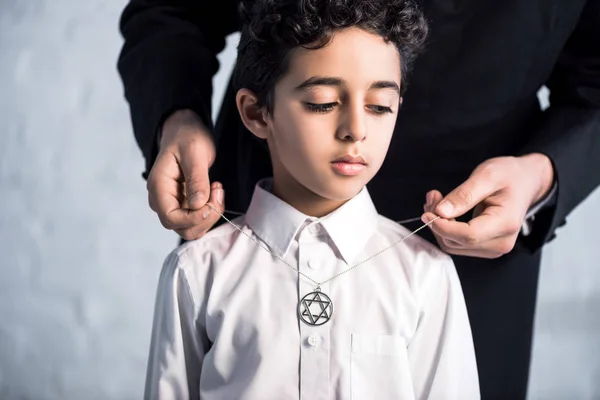 Cropped view of jewish father wearing star of david necklace on son — Stock Photo