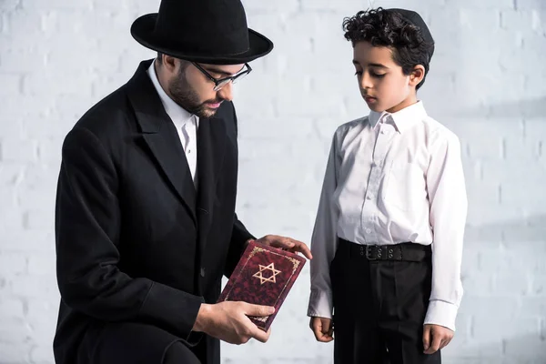 Hermoso padre judío sosteniendo tanakh y lindo hijo mirándolo - foto de stock