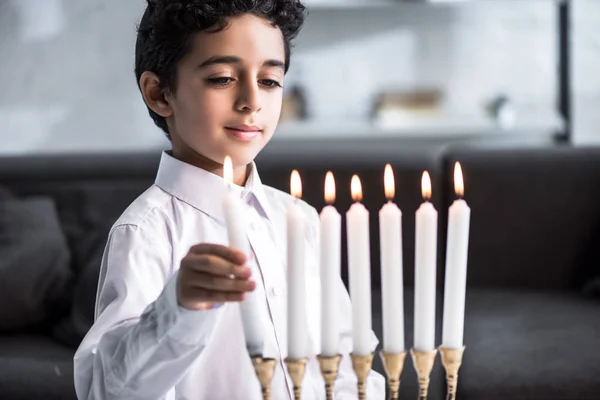 Lindo y sonriente chico judío en camisa sosteniendo vela - foto de stock