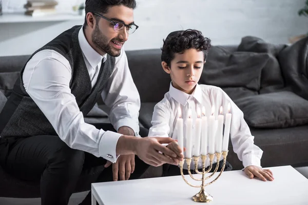 Sonriente padre judío e hijo sosteniendo vela en el apartamento - foto de stock