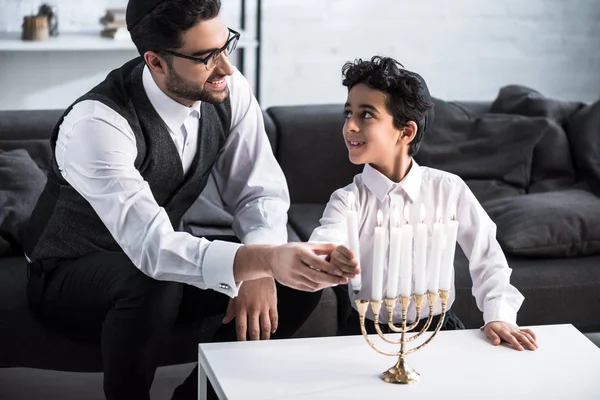 Smiling jewish father and son holding candle in apartment — Stock Photo
